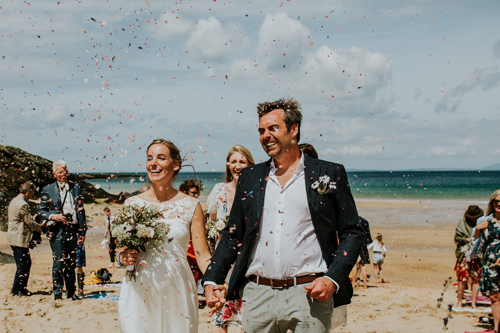 laughing bride and groom under thrown confetti on Kiloran Bay on the Isle of Colonsay