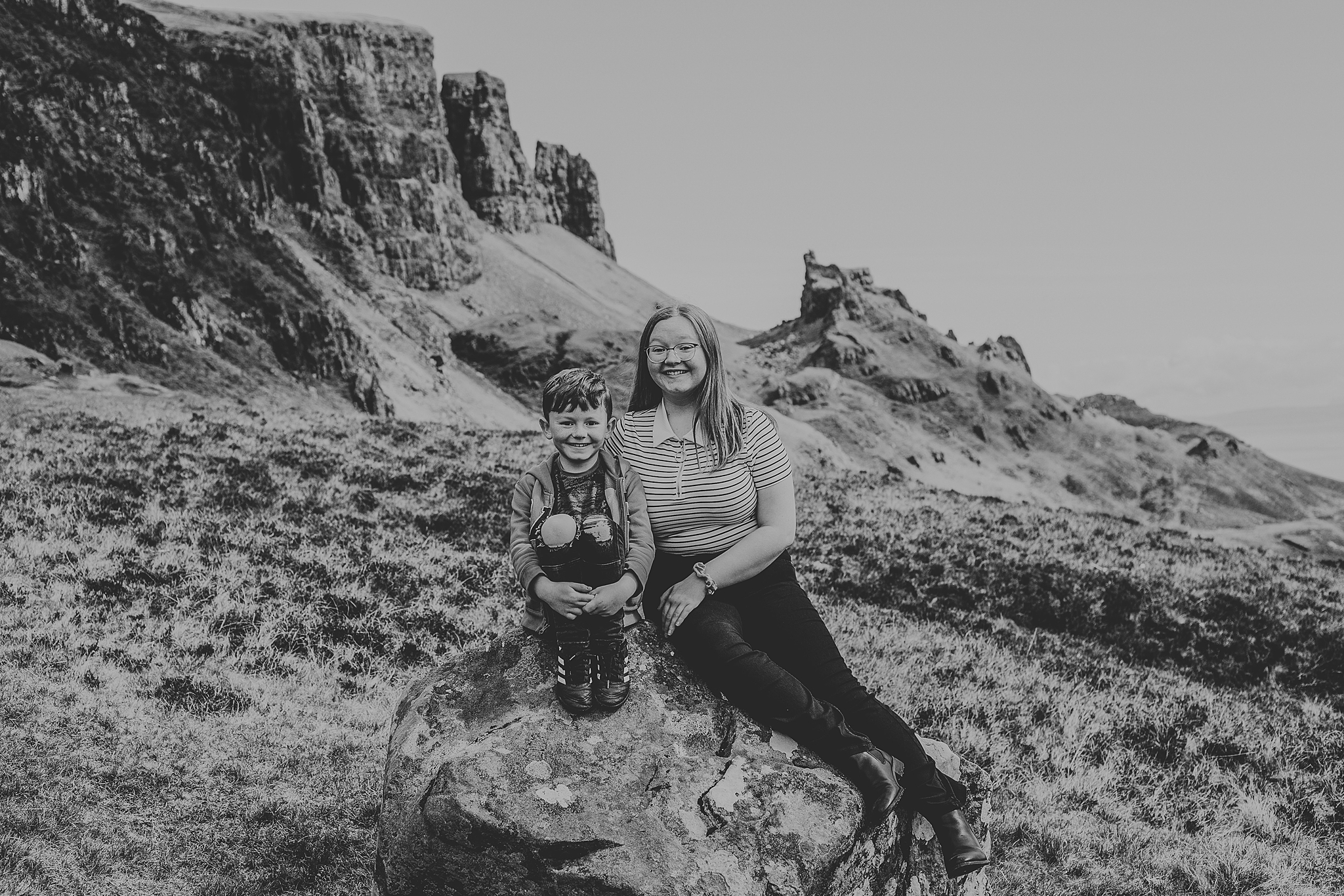 black and white photo of a brother and sister sitting on a rock at the quiraing on the isle of skye