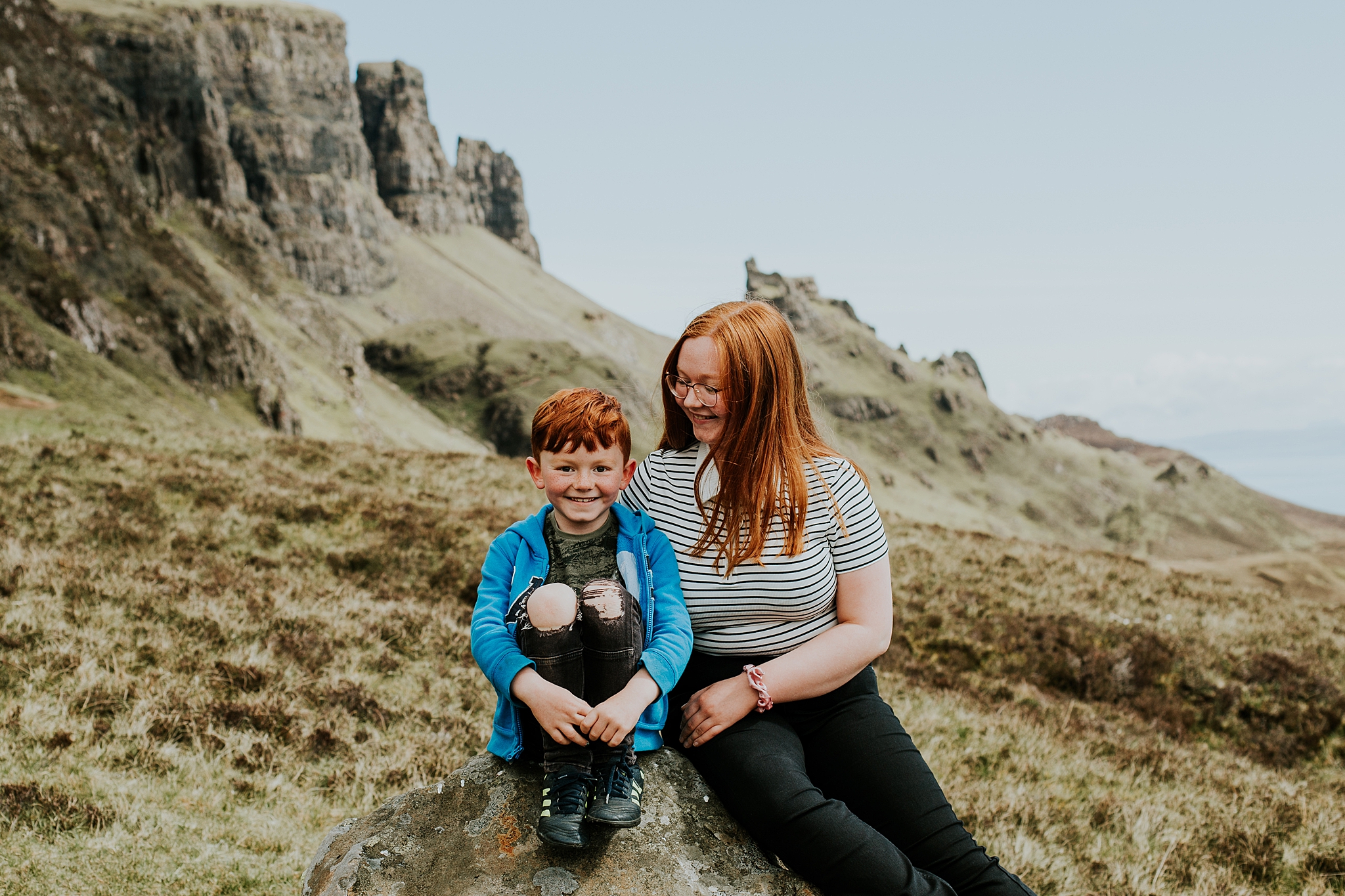 brother and sister smiling sitting on a rock at the quiraing on the isle of skye