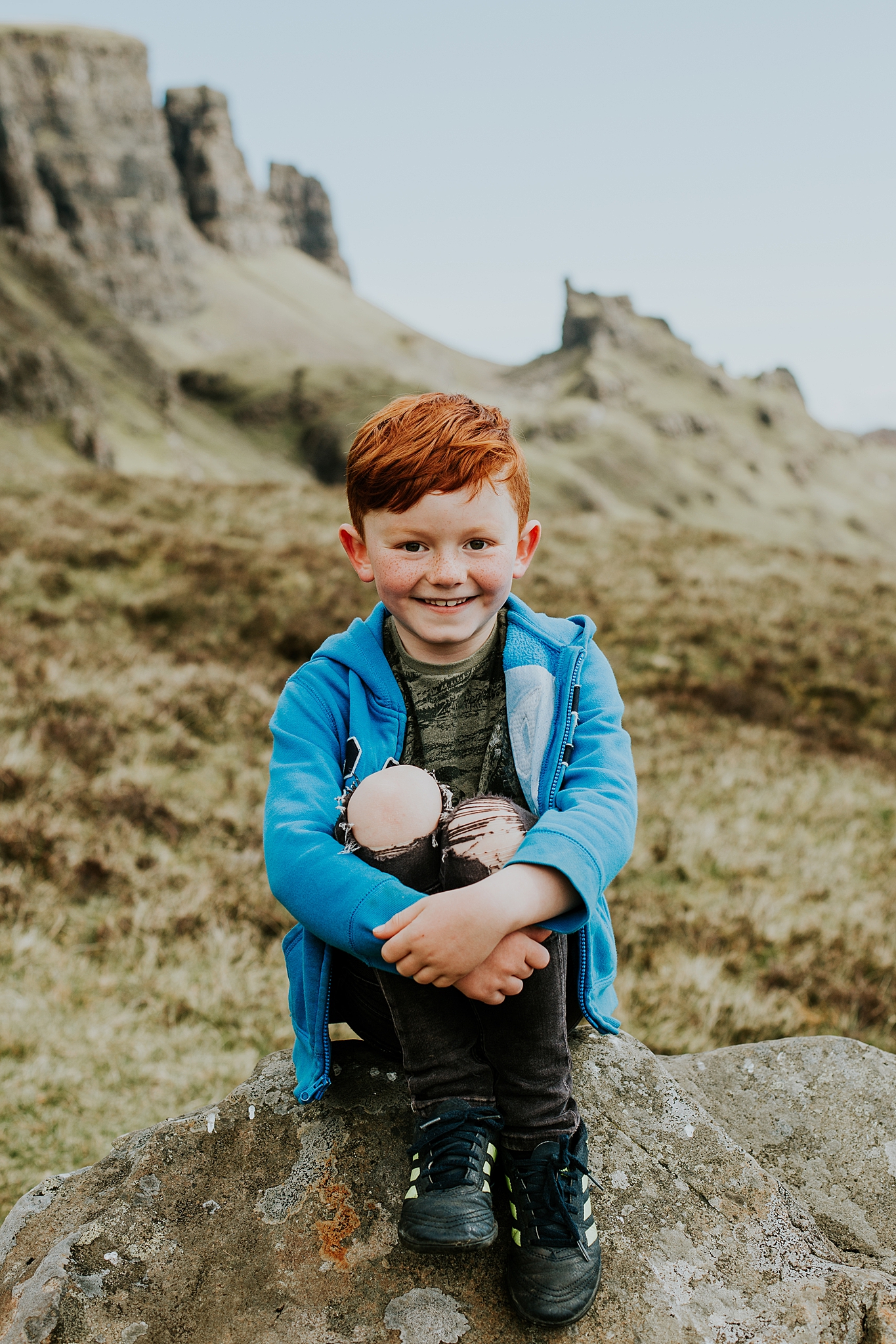 young red headed boy sitting on a rock smiling at the quiraing on the isle of skye