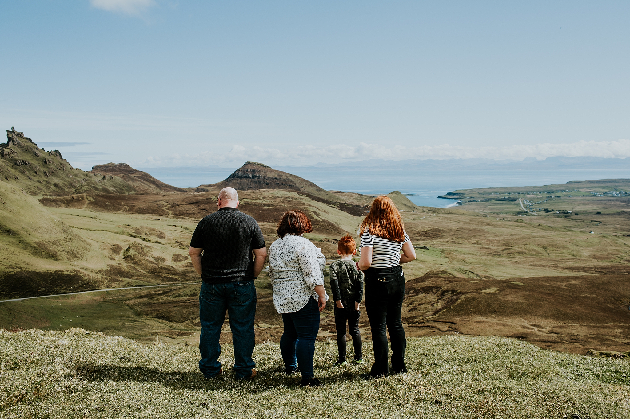 family of four with backs to the camera looking over a cliff at the quiraing on the isle of skye