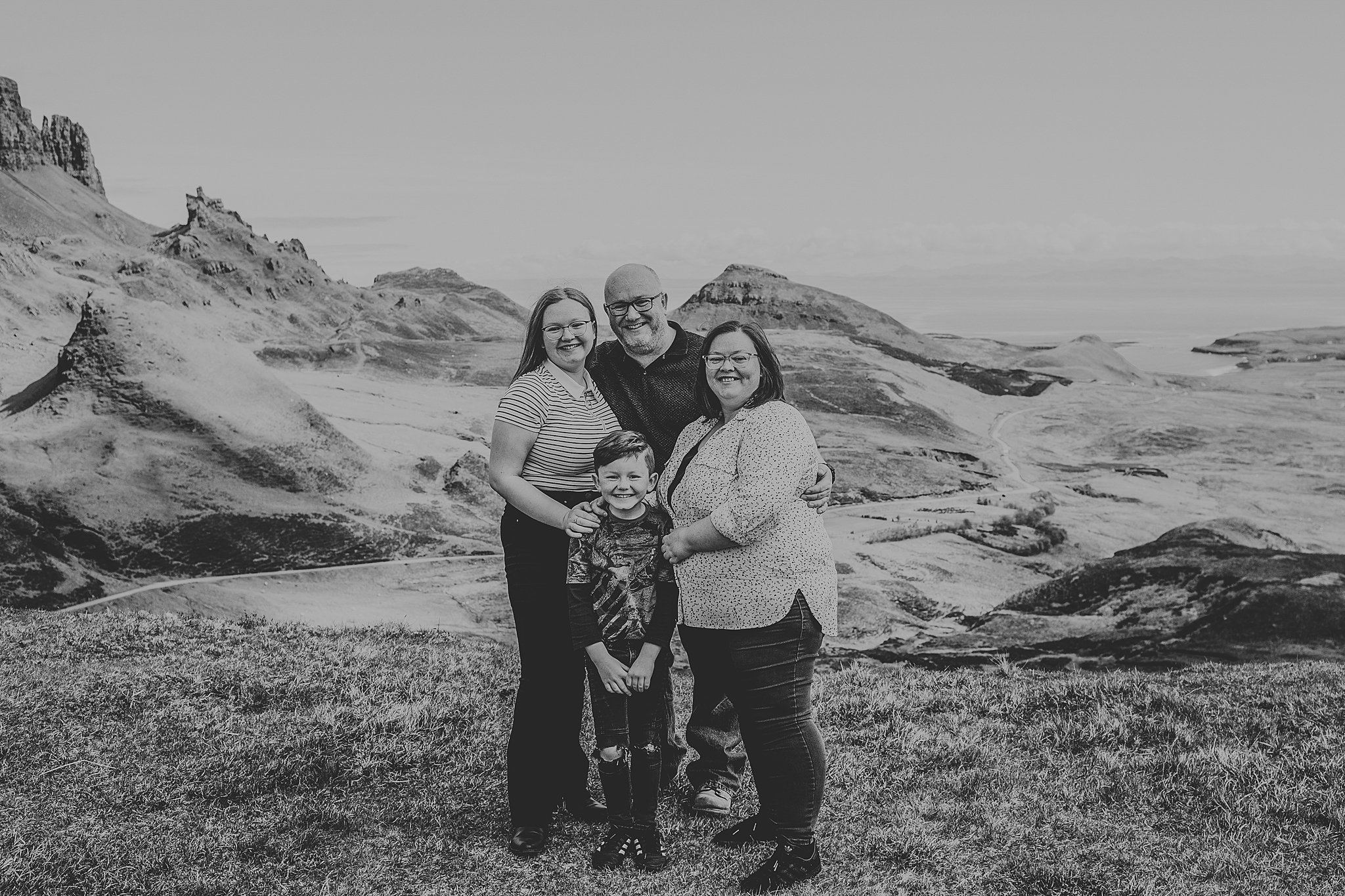 black and white photo of a family of four smiling at the camera at the quiraing on the isle of skye