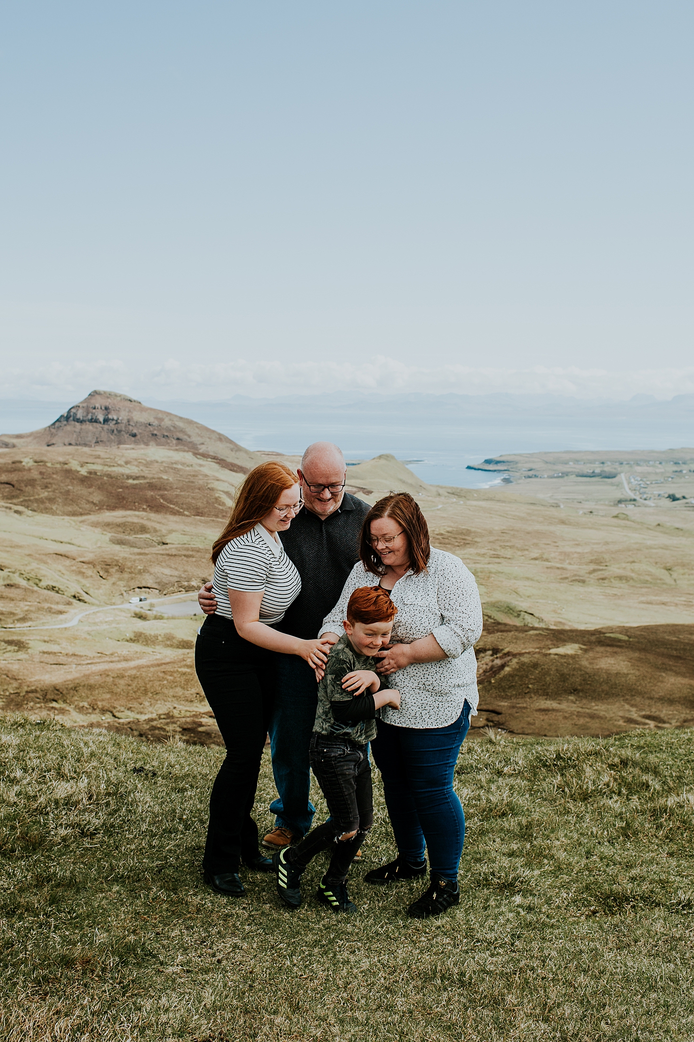 family of four huddled together tickling young red headed son all smiling at the quiraing on the isle of skye