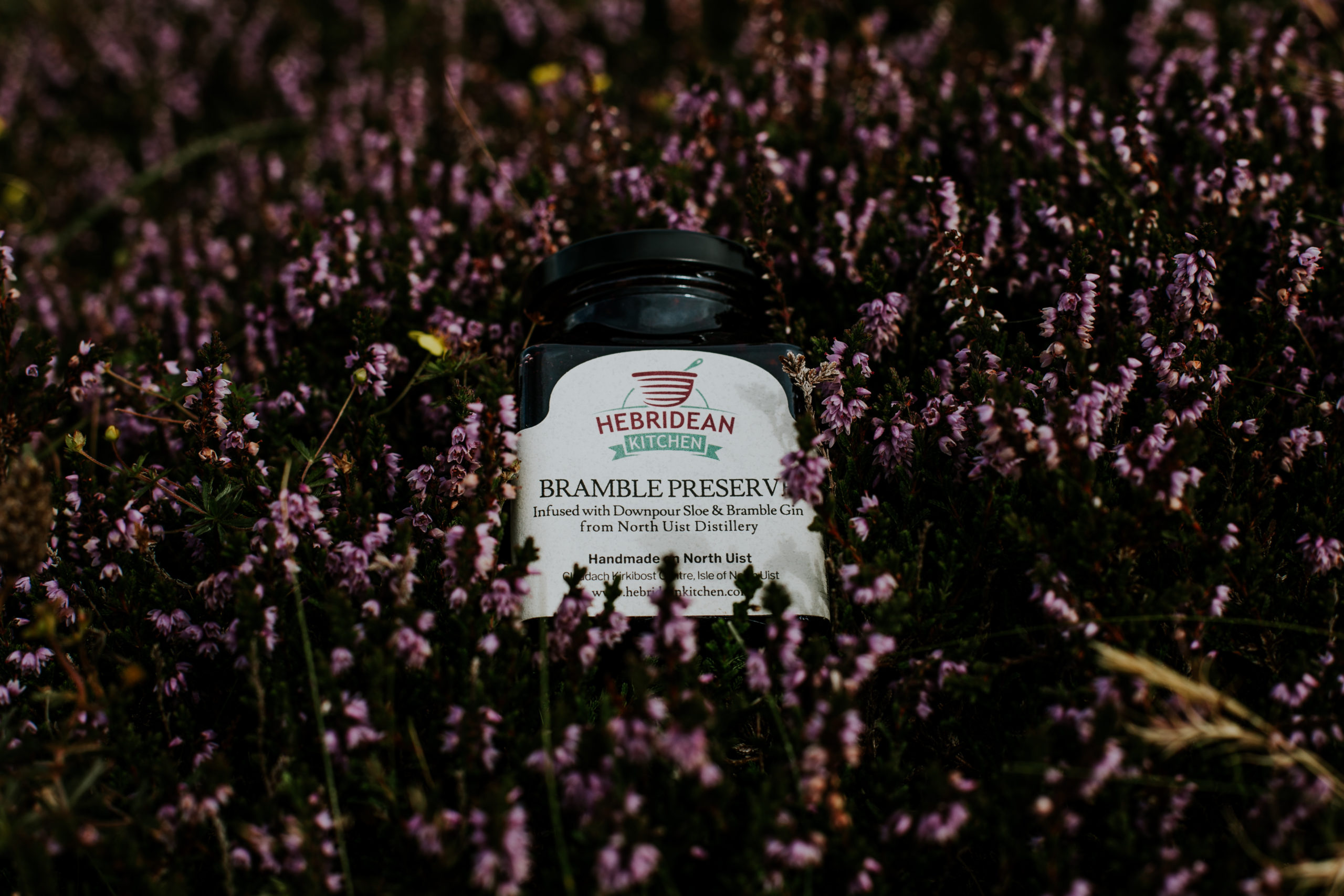 A jar of Claddach Kirkibost Centre Bramble Preserve nestled in some purple heather on the isle of North Uist